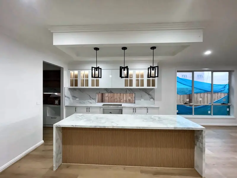 White kitchen with glass-front display overheads, a fluted timber island and marble-look tops, by Maya Cabinets in Melbourne