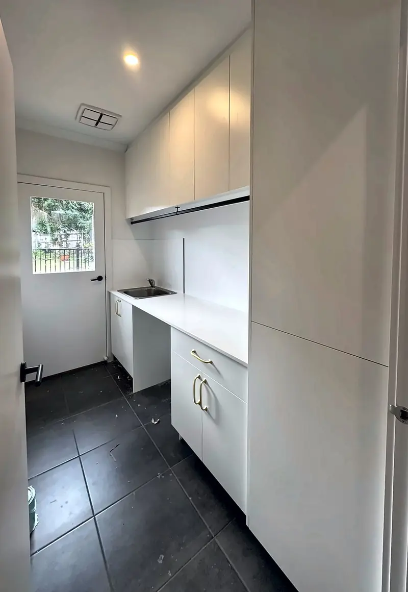 Laundry with a tall broom cupboard, overheads and a stone bench with a tub, by Maya Cabinets in Melbourne