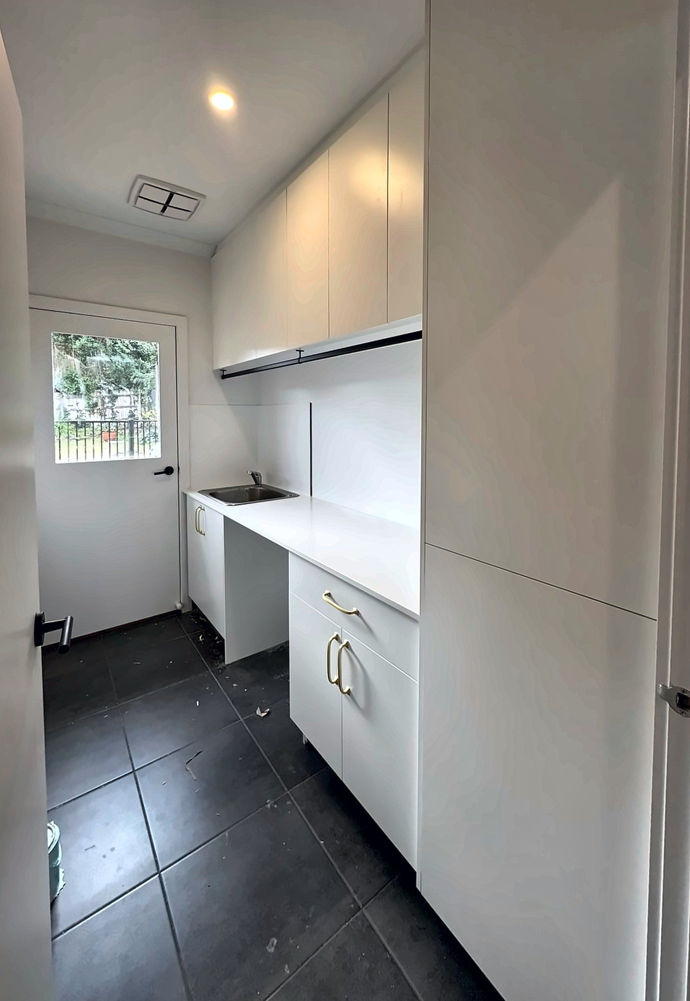 Laundry with a tall broom cupboard, overheads and a stone bench with a tub, by Maya Cabinets in Melbourne